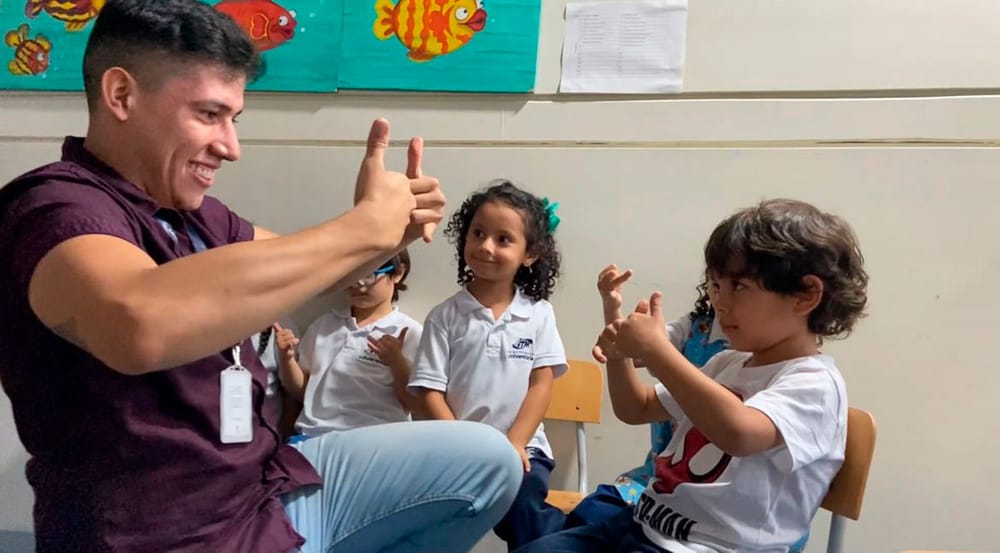 Docente enseña lengua de señas a niños en aula. Usan gestos con las manos y participan en actividad educativa inclusiva útil
